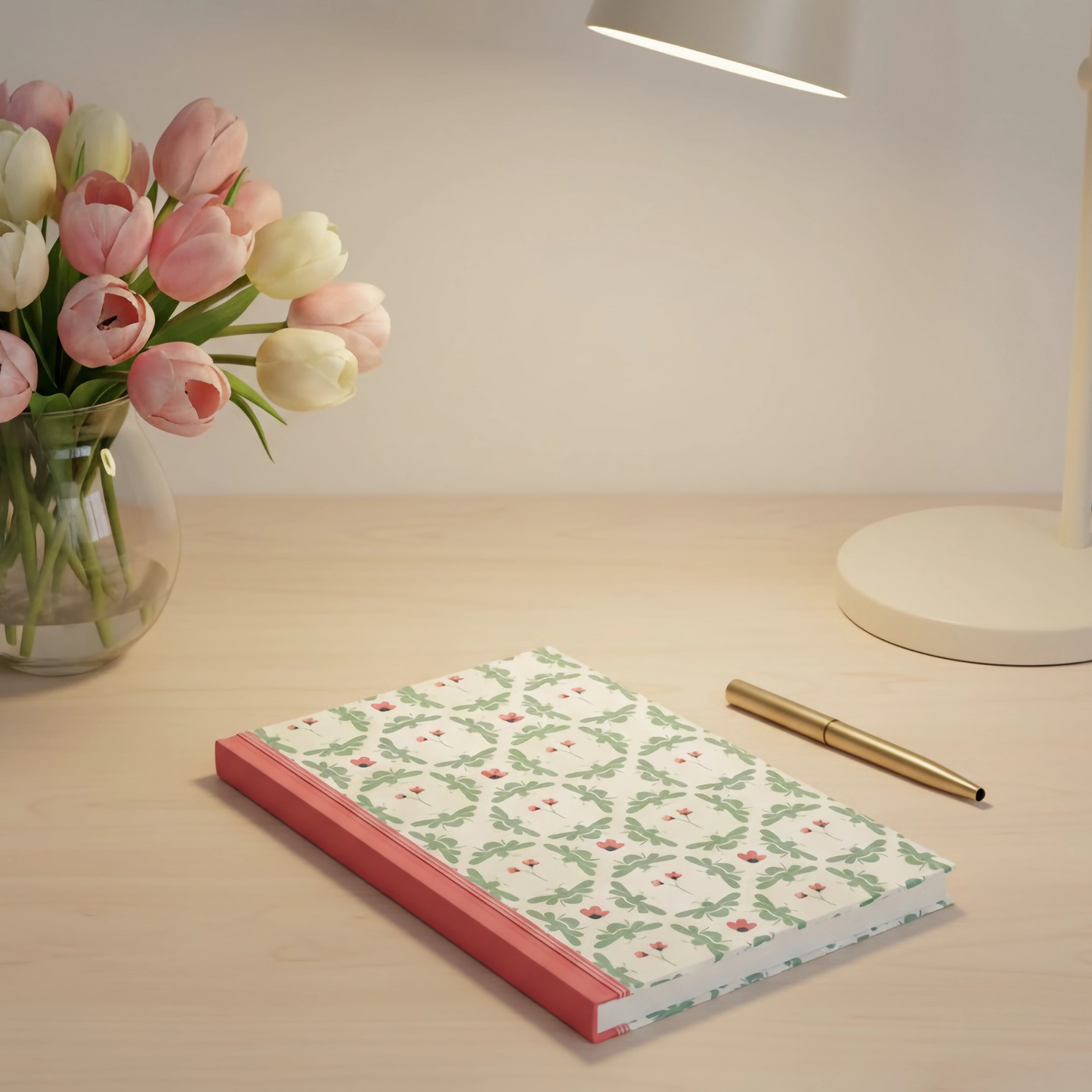 Notebook with floral design on a desk next to a vase of tulips and a pen.