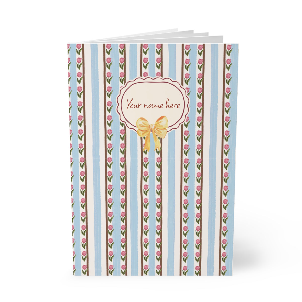 A personalized A5 softcover Notebook with a vertical striped pattern of light blue, white, and brown, decorated with pink tulips. A central cream-colored oval label features a gold bow graphic and the placeholder text 'Your name here'.